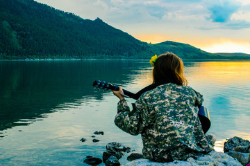 silhouette of a girl at sunset playing the guitar by the river