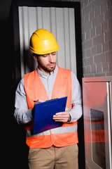 Handsome fireman looking at fire panel while holding clipboard and pen