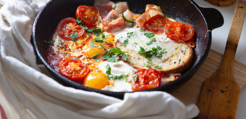 Fried eggs with bacon, toast and tomatoes in a pan