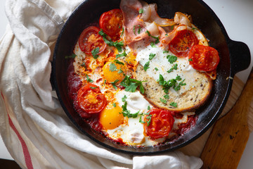Fried eggs with bacon, toast and tomatoes in a pan