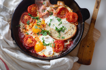 Fried eggs with bacon, toast and tomatoes in a pan