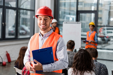 Cheerful fireman holding clipboard near coworkers giving talk on briefing