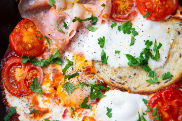 Fried eggs with bacon, toast and tomatoes in a pan