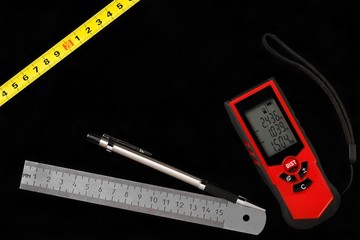 Tape measure, laser distance meter and metallic ruler with pencil on black background