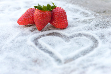 Three strawberries strawberries on sugar background with a heart drawn on it.
