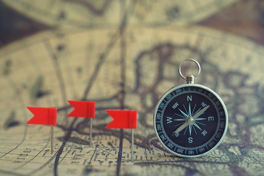 Old compass and flag marking pins on blur vintage map background, journey planning concept