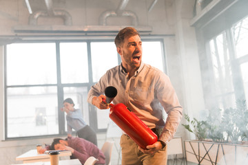 frightened businessman holding extinguisher and screaming in office with smoke near coworkers - obrazy, fototapety, plakaty