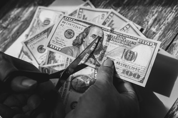 Man is cutting dollar banknotes with scissors on the purple pastel background. Money notes on the wooden surface. Devaluation of a currency. Business and society problems.