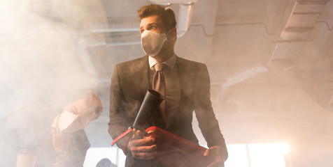 scared businessman in mask holding extinguisher near coworker in office with smoke