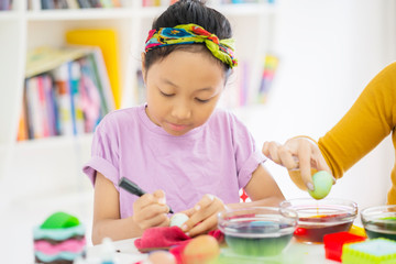 Asian little girl learns to dye eggs with her mother