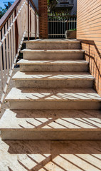 White marble staircase of an Italian house, with white and brown iron railing. Orange brick wall.