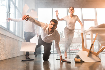 scared businessman falling on floor while running and screaming near coworkers in office with smoke