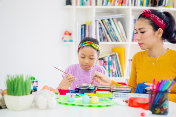 Asian woman and her daughter colors Easter eggs