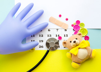 Children`s doctor appointment date number concept. Calendar with numbers, doctor, kids toys, pink and green buttons. Flat lay view.