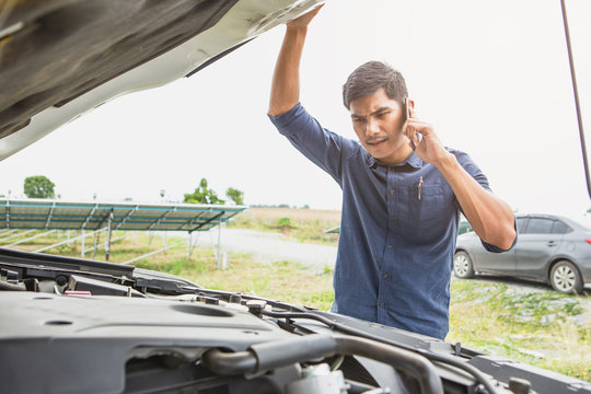 Stressed man having trouble with his broken car looking in frustration at failed engine.Driver on the road having problem with a car. Young man calling for help with the mobile phone.