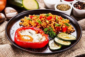 Fried egg, groats and vegetables on wooden table