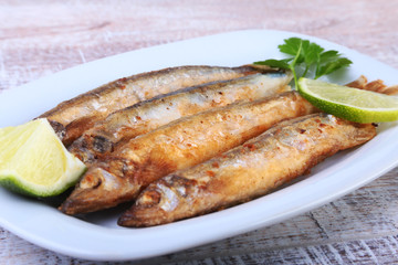 Deep frying small fish capelin and sliced lemon on white plate. Good snack to beer.