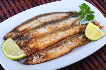 Deep frying small fish capelin and sliced lemon on white plate. Good snack to beer.