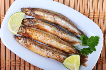 Deep frying small fish capelin and sliced lemon on white plate. Good snack to beer.
