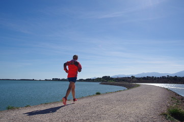 Coureur en short qui fait du footing le long de la mer et la montagne