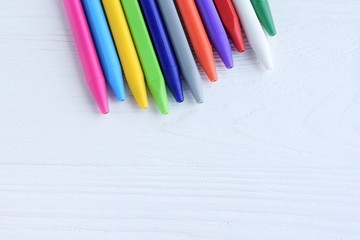 Bright colorful pens with selective focus on white wood textured background with empty space. Back to school flat lay. Row of rainbow pens on wooden backdrop. Multicolored education tools for art