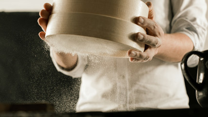Flour sieve in male chef hands in the kitchen