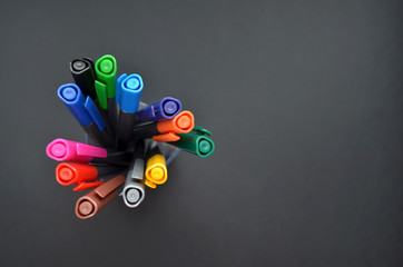 Set of multi-colored bright pens standing in a transparent glass, top view on black background, closeup with copyspace