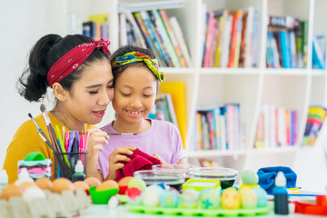 Little girl guided by her mother to dye Easter eggs