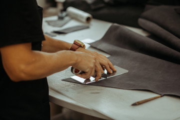 Close up of an artisan working with leather in his laboratory using tools. Handmade concept. Man holding crafting tool and working.