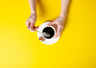 Cup of coffee with chocolate pieces in hand on yellow background, top view