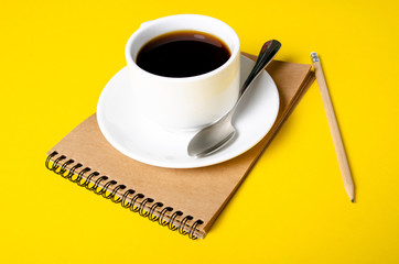 Cup of coffee, notepad, pencil on yellow background