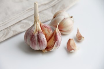 The head of garlic is broken and is on a light background. There are a few cloves of garlic and a napkin.