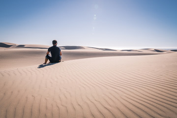 Man sitting in the Desert / Dune looking out in the scene