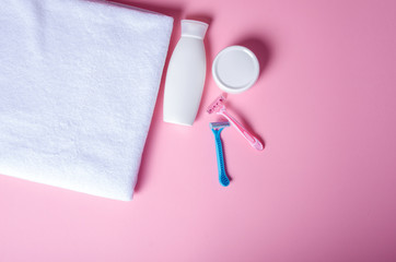 White towel, jar cream, lotion, razor, roller deodorant soft beauty on pink background, top view