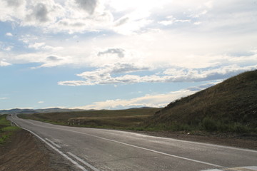 road in steppe under a blue sky with white clouds Sayan mountains Siberia Russia
