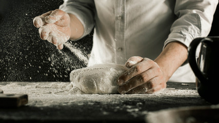 Male chef hands knead dough with flour on kitchen table