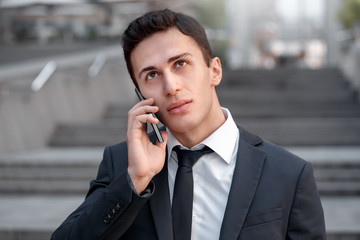Business lifestyle. Businessman standing on the city street talking on smartphone pensive close-up