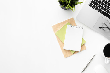 White office desk table with blank small notebook, laptop computer and supplies. Top view with copy space, flat lay.