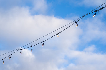 Lightbulbs strung with wire, illuminated, against a blue sky with clouds