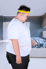 Overweight man measures his belly in the bedroom