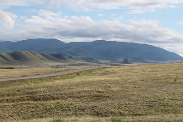 Fototapeta na wymiar Wide steppe with yellow grass under a blue sky with white clouds Sayan mountains Siberia Russia
