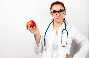 A young doctor with a stethoscope, with glasses holding an apple in her hand