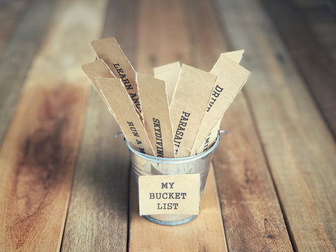 Motivational and inspirational concept - My Bucket List written on paper. There are list of wishes written on papers and placed inside the bucket. Blurred vintage styled background.