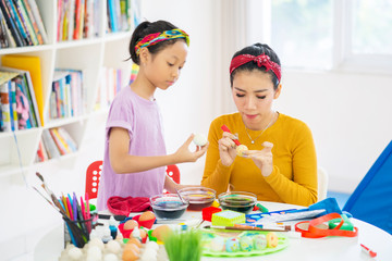 Young mother teaches her daughter to paint eggs