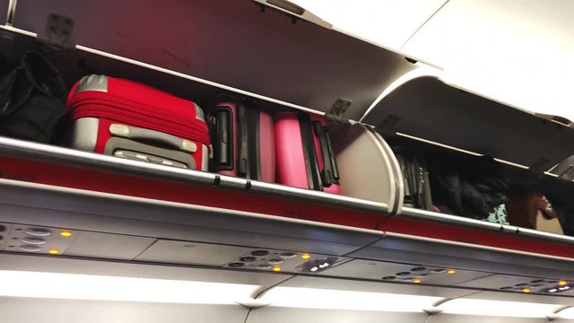Close-up of bright suitcases lying on the shelves in the plane. Economy class cabin of typical airliner.