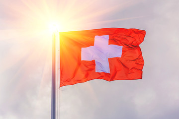 The national flag of Switzerland flutters in the wind against a blue cloudy sky.