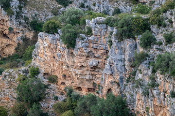 Fototapeta na wymiar Distant soft colors landscape view of the arched entrances of caves near the ancient town of Matera, the Sassi di Matera, Basilicata, Southern Italy, cloudy summer afternoon just before sunset