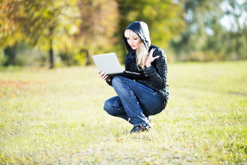 Naklejka na ściany i meble Young woman with laptop in autumn park