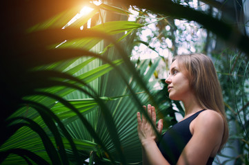 Portrait of cute young woman meditating and doing namaste hand in jungle. Sunny day