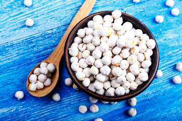 Bowl and spoon with dry chickpeas on wooden table.